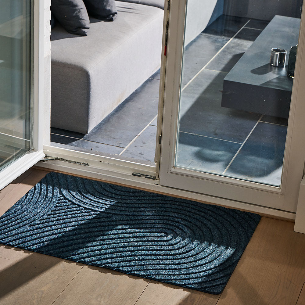Lifestyle photo showcasing WaterHog All-Weather Indoor Outdoor blue navy marine colour Floor Mat in use in front of door at a terrace with a seat and pillows and an open door